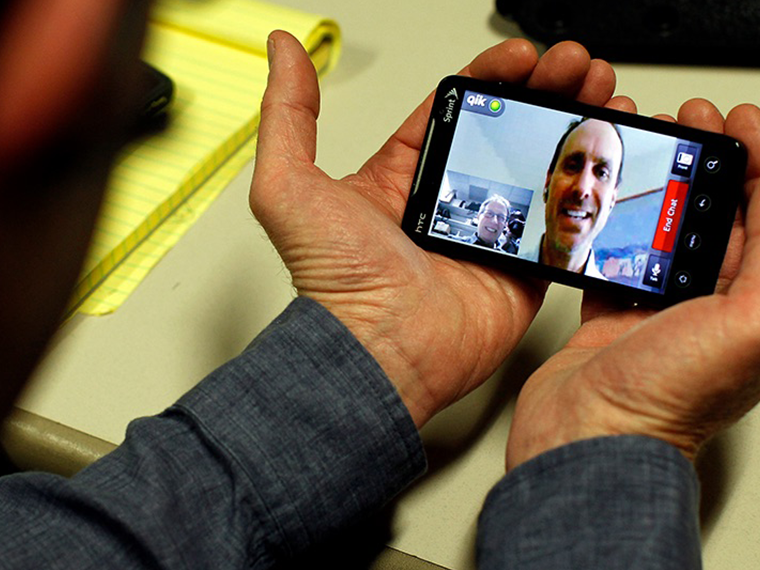 Two hands holding a phone displaying a man on a video call