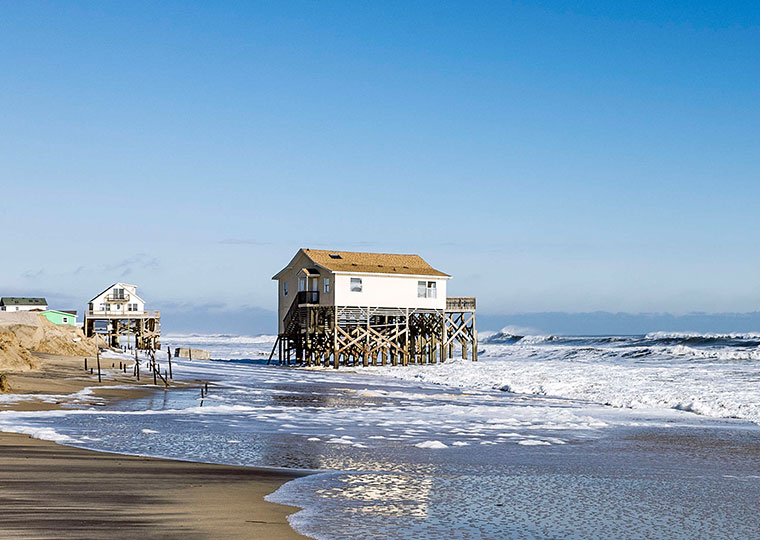 A view of a white house on stilts on a beach shore