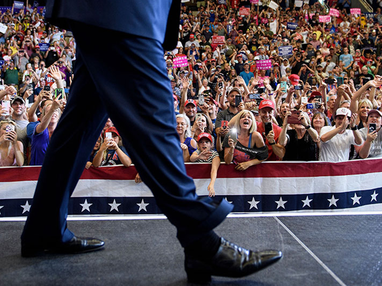 An unseen American politician walking on their stage at a rally