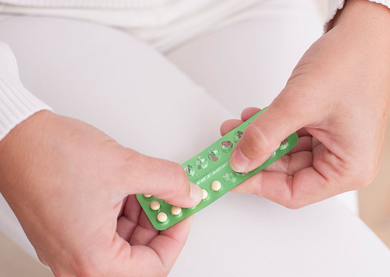 Two hands push medication out of a green plastic container