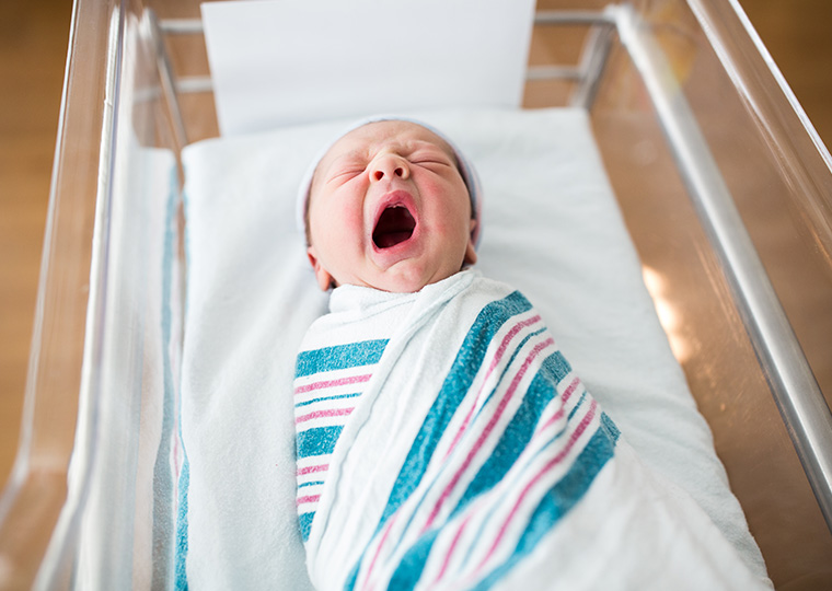 Image of yawning newborn baby in bassinet