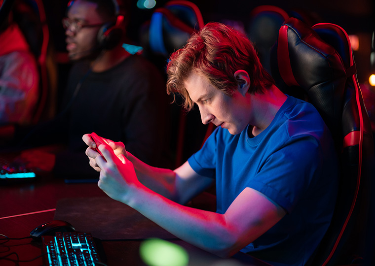 A young man wearing a blue shirt plays a game on his cellphone
