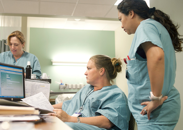 Three nurse confer in front of a computer screen at a nurses station