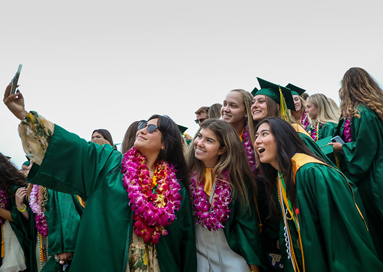 Three girls in green graduation gowns take a selfiea