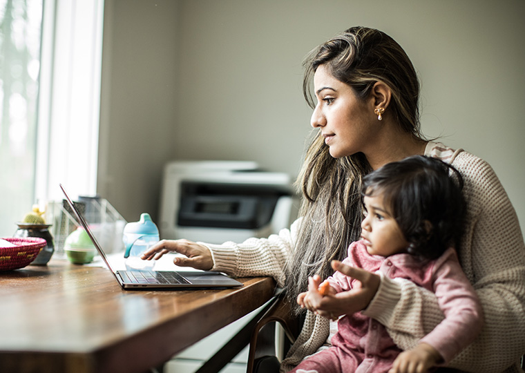 A women sitting in front of her laptop holding her toddler daughter
