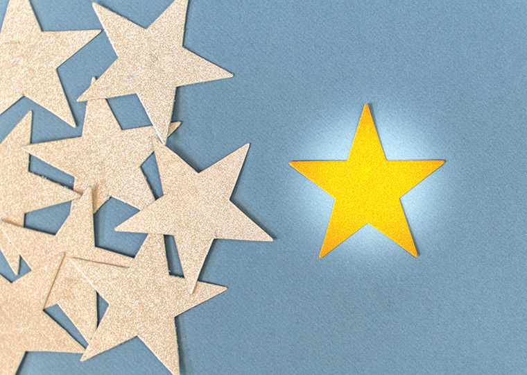 A pile of glittery gold stars on the left of the frame and in the center a yellow star