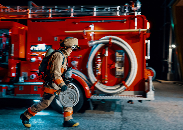 A firefighter in gear carries a fire hose as they walk past a fire truck