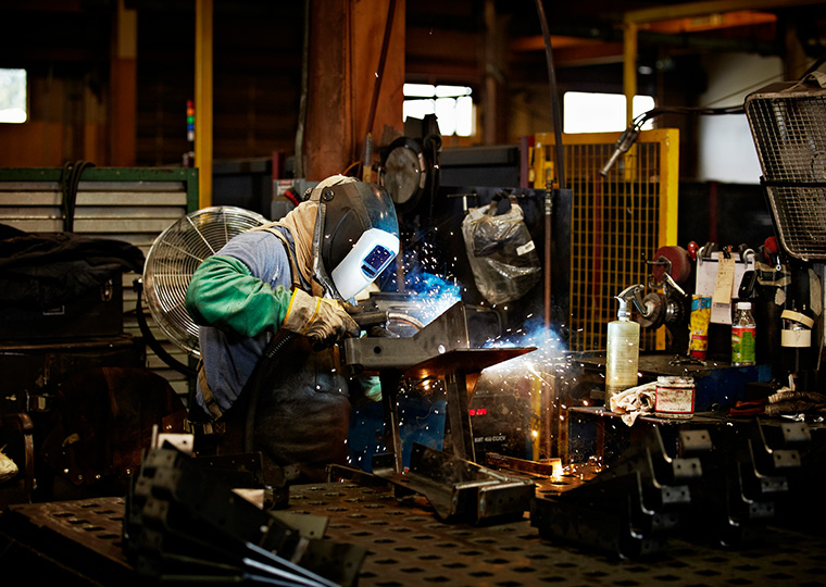 A welder wearing protective head gear works on a piece of metal in a workshop