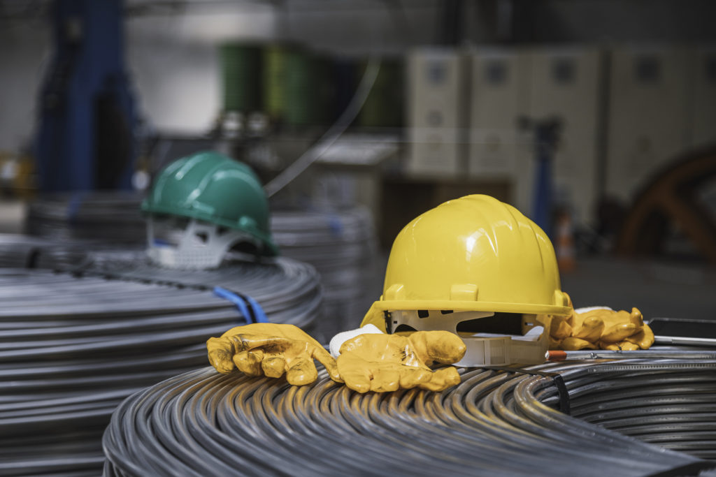 Yellow and green work helmet and protective gloves on steel cable equipments in a factory.