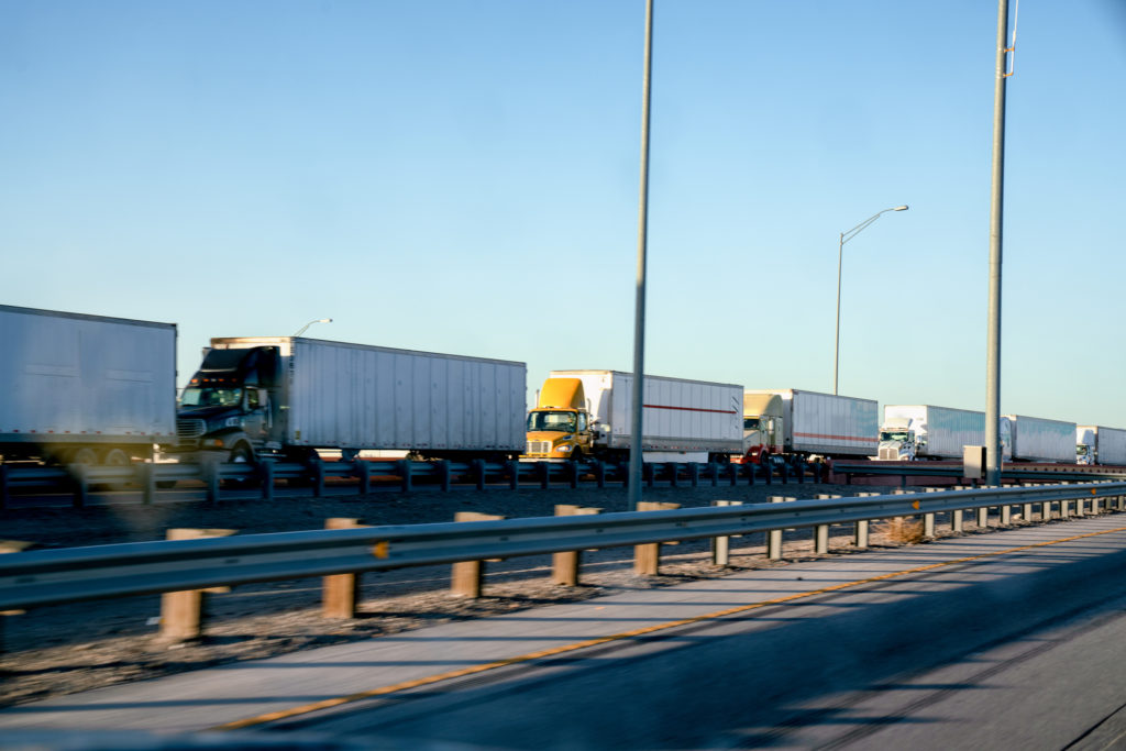 A long line of semi-trucks waiting at the U.S. side of the international border crossing into Mexico to transport goods.