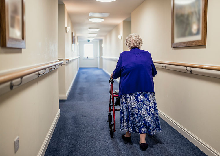 A senior woman walking down a corridor with the assistance of a walker. view from rear.