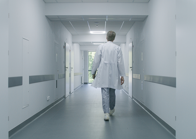 Mature doctor walks down hospital corridor with digital tablet computer. 
