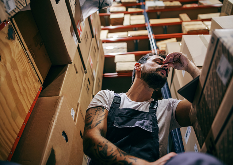 Tattooed bearded worker in overalls sitting in the storage area of import and export firm interior after having hard day at work.