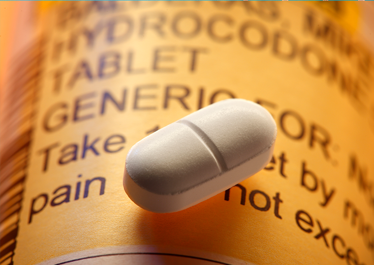 A close-up of a single opioid pill resting on top of a prescription pill bottle.