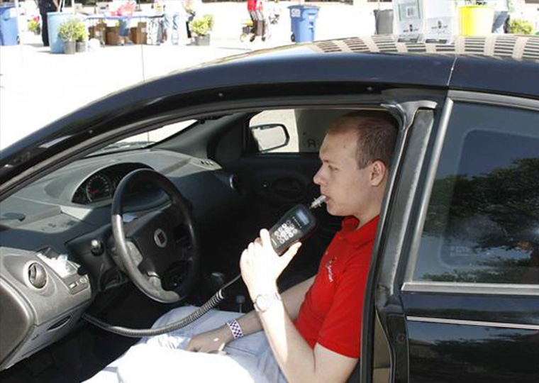 A man is seated in his car is using an ignition interlock, which is a breath test device linked to a vehicle’s ignition system.