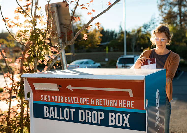 A woman deposits her vote in a sealed envelope into an official voting ballot box in Washington state.