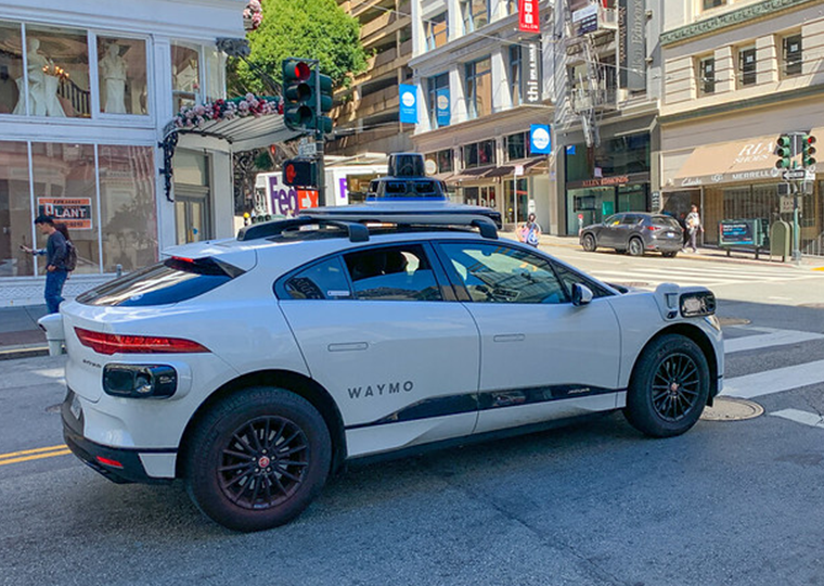 A white Waymo autonomous vehicle on the street near a crosswalk.