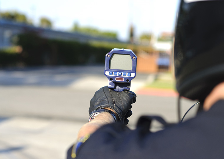 The back of helmeted police officer holding a radar gun.