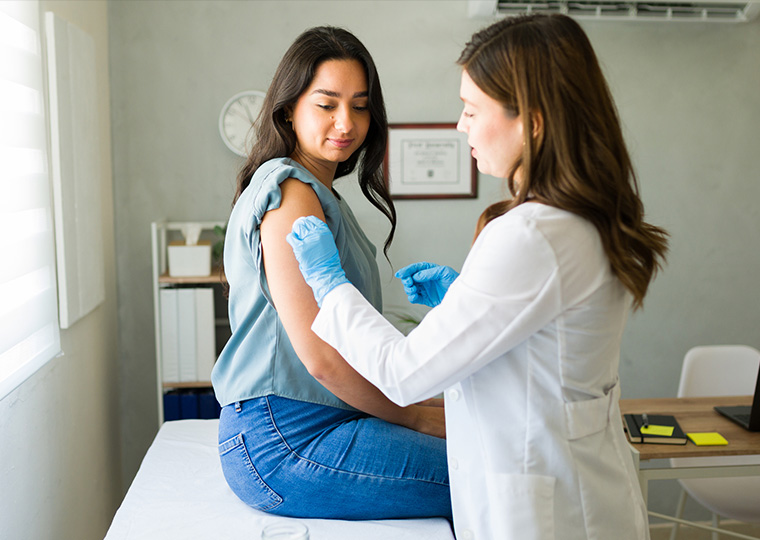 Young Hispanic woman is getting vaccinated by a professional medical worker wearing gloves in a doctor's office