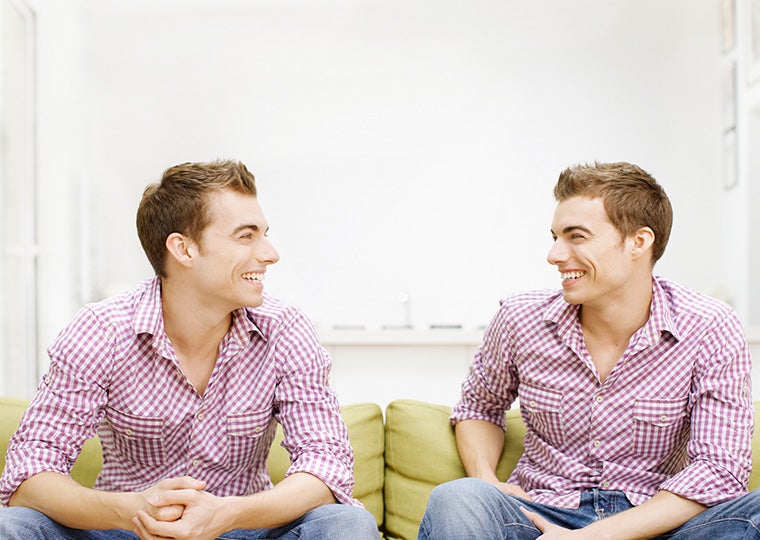 Twin brothers sitting on sofa, facing each other, smiling
