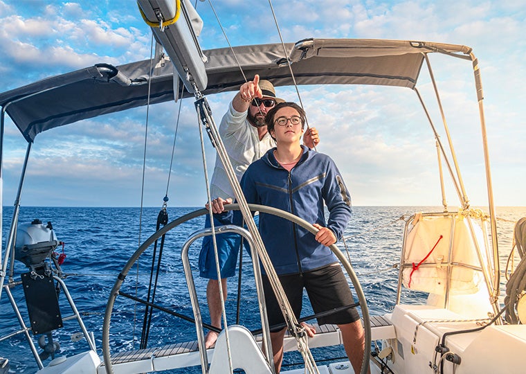 A father teaches his son to sailboat and guides him.