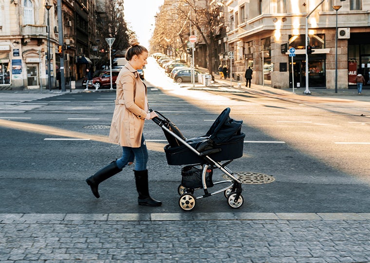 Side view of Young Caucasian mother enjoying with her little baby relaxing in his baby carriage