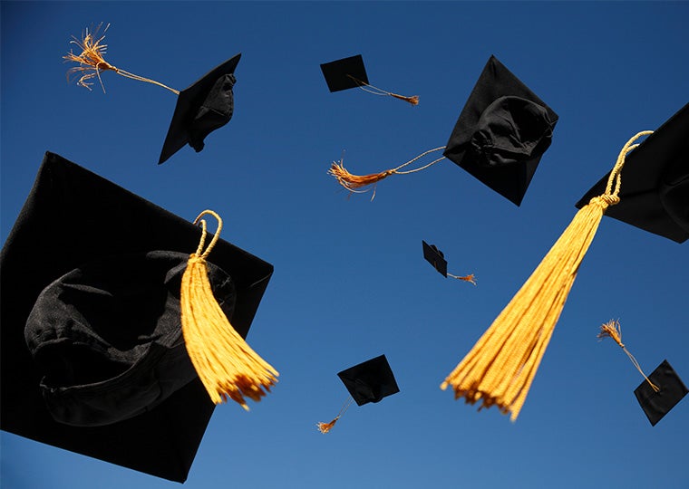 Black graduation caps with gold tassels thrown in the air